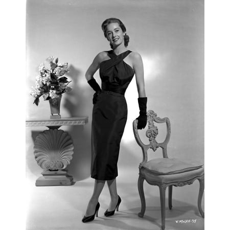 Vera Miles posed standing in a black ankle length halter dress and gloves while leaning onto a chair back with her hand propped onto her hip Photo
