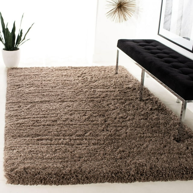 SAFAVIEH Polar Abbot solid taupe plush shag area rug displayed in bright room with black tufted bench and green potted plant.