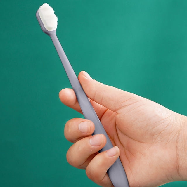 fiudx cepillo de dientes suave, limpieza delicada de las encías con cabezal ondulado y mango cómodo; cepillo blanco con mango gris sostenido en mano sobre fondo verde, vista 3/4 que muestra filamentos densos y cabeza compacta, apto para uso diario y viajes, también suele usarse para limpieza suave de retenedores.