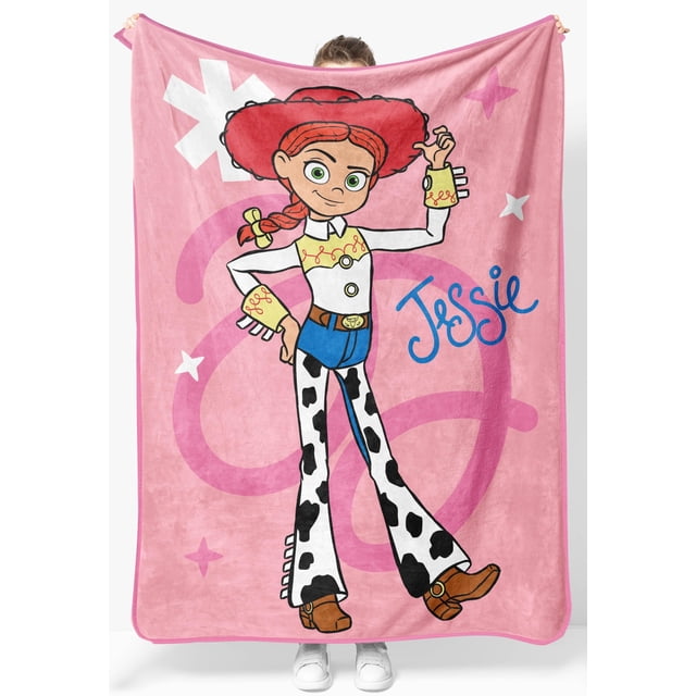 manta ligera toy story jessie 117 x 152 cm jay franco Manta throw con gran estampado de Jessie de Toy Story sobre fondo rosa; vista frontal centrada con figura completa de Jessie (sombrero rojo, blusa blanca, pantalón tipo vaca y botas marrones) y texto decorativo «Jessie» en azul; microfibra fleece de superficie lisa, bordes cosidos, medidas 117 x 152 cm; adecuada para sofá, cama o llevar de viaje.