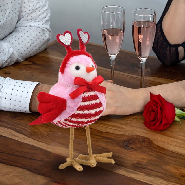 decoraciones para san valentín, adornos para san valentín, regalos para san valentín, decoración para san valentín, adorno para san valentín, muñeco enano, muñeco de pájaro para san valentín. Figura de pájaro de polyester color PK (rosado y rojo), 20×15×8 cm, vista frontal centrada; pecho con rayas de lentejuelas rojas y blancas, lazo rojo en el cuello, antenas con corazones brillantes, pico naranja y patas forradas beige; sobre mesa de madera junto a dos copas con bebida rosada y una rosa roja. A menudo usada como adorno de mesa o complemento para regalos románticos.