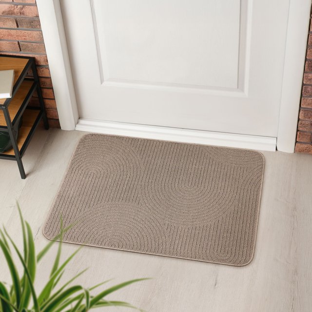 Mainstays Chai Tufted Archlink Tufted Washable Kitchen Mat 20x30 inches in sand beige with a mid-century modern archway pattern, loop-pile texture, and eco-friendly TPE non-slip backing, placed on light wood flooring in front of a white door, machine washable for easy care and suitable for kitchen comfort.