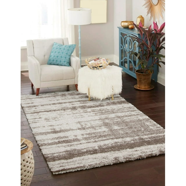 Contemporary plush and shag ECARPET Brindle area rug with gray and white pattern on dark hardwood floor in a stylish living room featuring beige armchair, blue cabinet, white fluffy ottoman, floor lamp, and potted plant.