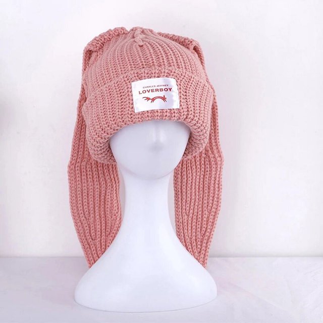 gorro de orejas largas de conejo para hombre y mujer, gorro cálido de punto con letras, unisex rosa. Vista frontal centrada sobre busto blanco; doblez en la frente con etiqueta blanca con letras visibles, orejas largas tejidas que caen a los lados, textura acanalada de mezcla de algodón, apto para uso casual e invierno y para fiestas como Pascua o Navidad.