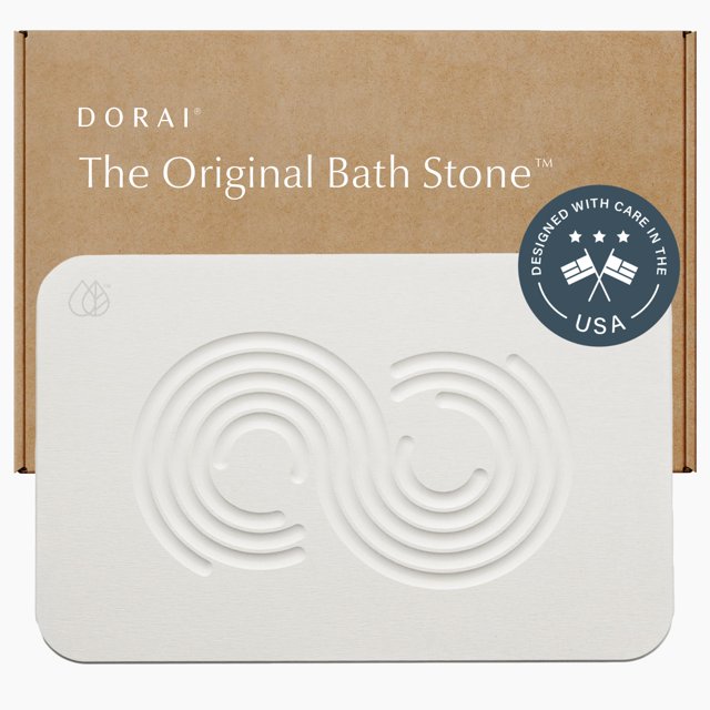 dorai home alfombra de baño de piedra de 23,6 x 15,4 pulgadas, alfombrilla de baño de piedra de diatomita antideslizante de secado rápido para baño, piedra arenisca zen. Vista frontal centrada de la alfombrilla rectangular color arenisca zen con esquinas redondeadas; superficie lisa tipo piedra con dos diseños concéntricos en relieve y logo en la esquina superior izquierda; borde inferior indica base antideslizante visible sobre una caja de cartón marrón al fondo; adecuada para colocar frente a la ducha o tina.