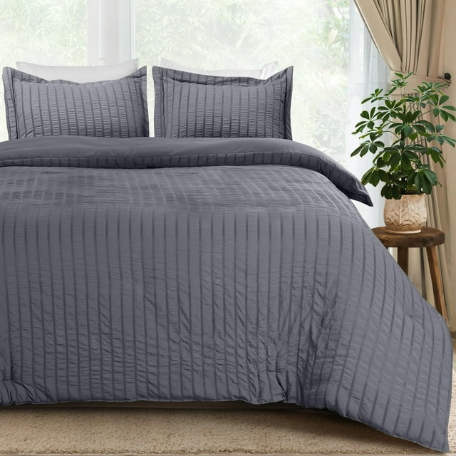 juego de funda nórdica utopia bedding queen size seer sucker, gris funda nórdica queen de microfibra gris con diseño de rayas de sirsaca, vista frontal centrada mostrando la silueta completa y la textura vertical, cremallera cerrada y dos fundas de almohada a juego detrás en dormitorio luminoso con cortinas y mesa auxiliar con planta; suele usarse para renovar rápidamente el look de la cama.