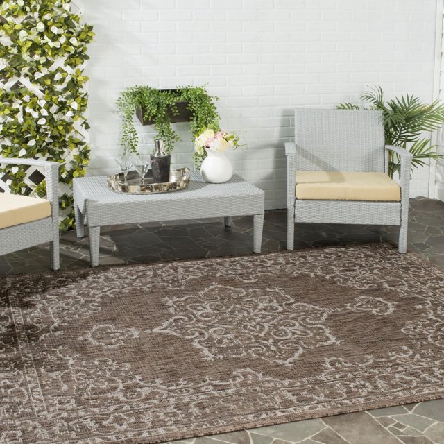 SAFAVIEH Courtyard Clodagh Medallion indoor/outdoor area rug in brown with beige intricate medallion pattern displayed in patio setting with gray wicker furniture
