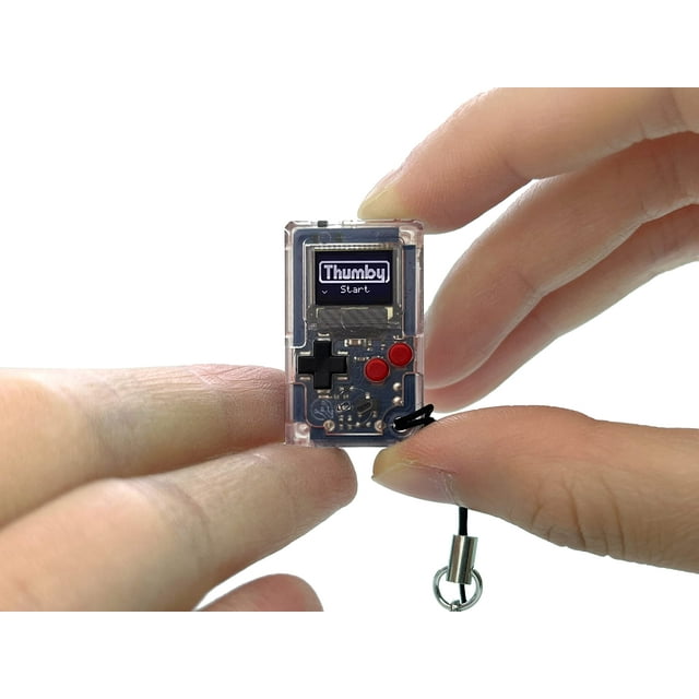 Tinycircuits Thumby (clear) tiny game console, a miniature playable and programmable keychain, shown held between fingers. Features a clear casing, six functional buttons, and a small screen displaying 'Thumby Start.' Preloaded with retro games, it includes a keychain attachment for portability and STEM learning applications.