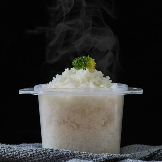 olla arrocera al vapor perfecl para microondas 900ml vaporera multiusos arrocera blanca de 900 ml, vista frontal centrada del recipiente translúcido con línea de nivel y asas planas, tapa con colador integrada; arroz cocido y humeante sobresale por la tapa con un trozo de brócoli encima, fondo negro y paño gris; apta para cocinar arroz, pasta y verduras en microondas, suele usarse también para escurrir y refrigerar porciones pequeñas.