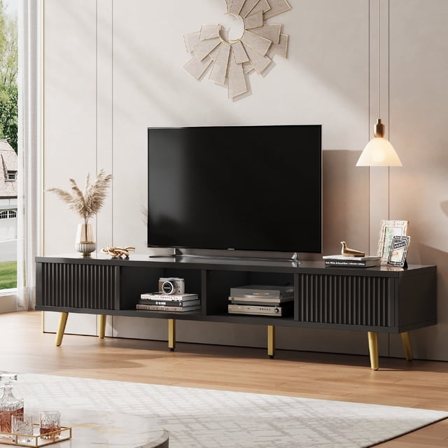 Bestier Meuble Télé Cannelé de 71 Pouces pour Téléviseurs jusqu'à 75 Pouces, Centre de Divertissement Moderne Noir à Fini Très Lustré avec Panneaux de Porte Cannelés Effet Vague, Profil Courbé et Pattes Dorées chic. Comprend Deux Grandes Armoires de Rangement avec Portes Coulissantes et Étagères Ouvertes pour Appareils Multimédias, consoles de Jeu et Déco. Comprend des Trous de Gestion des Câbles pour une Installation Propre. Positionné dans un Salon Lumineux avec un Téléviseur Monté et des accents Décoratifs.