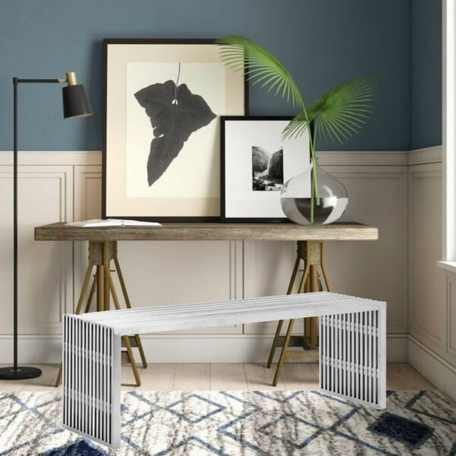 Large Vixey metal bench in brushed chrome finish placed on patterned rug in modern entryway with wooden table, framed art, and floor lamp.
