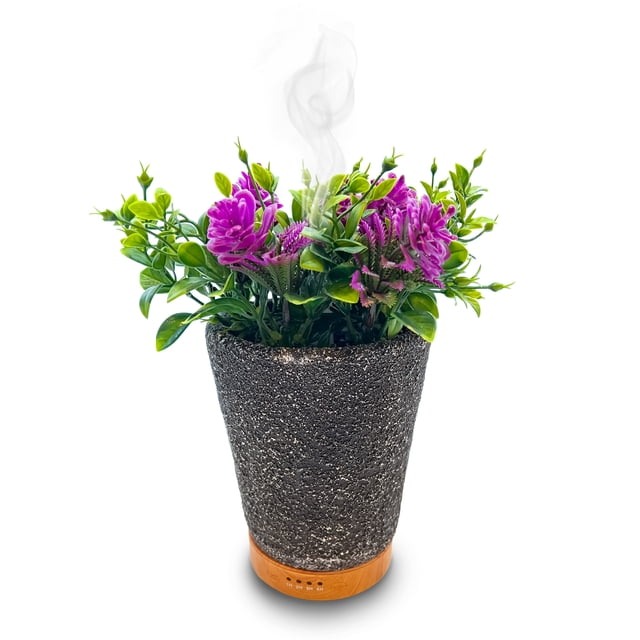difusor de aceites esenciales antava pro base de bamboo humidificador ultrasonico 200 ml planta flores, vista frontal centrada de un difusor tipo maceta con cuerpo texturizado gris y anillo de bambú en la base; flores y follaje artificiales morado y verde que aparentan realismo según especificación; vapor fino emergiendo del centro, adecuado como ambientador para aromaterapia y spa en el hogar.