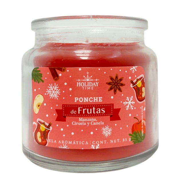 Vela Holiday Time Ponche De Frutas 85 G en frasco de vidrio transparente con cera roja y etiqueta navideña que indica aroma a manzana, ciruela y canela, ideal para decoración y ambientar espacios pequeños con fragancia cálida y duración de 20 horas, también adecuada para reutilizar el frasco.