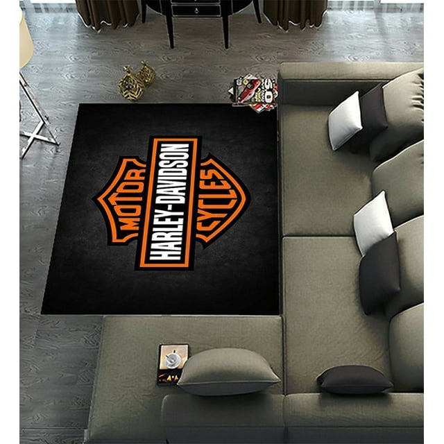 DEYOU Harley Davidson Motorcycles Pattern Area Rug, measuring 6 x 9 feet, displayed in a modern living room setting. The rug features a bold Harley Davidson logo in orange and white on a black background. Made of ultra-fine fiber polyester fabric, it is soft, water-absorbent, and includes a silicon dioxide anti-skid pad for safety. Suitable for various indoor spaces such as living rooms, bedrooms, kitchens, and offices. Machine washable for easy care.