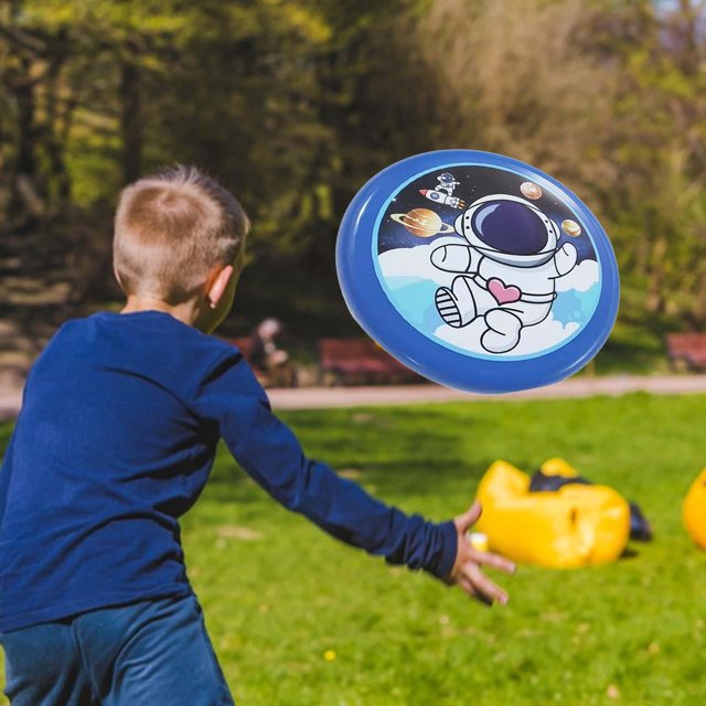 platillos voladores juego de actividades al aire libre para lanzar a mano para niños evitación de platillos voladores Platillo volador azul con dibujo de astronauta en vista 3/4, 20 cm (7.87 in) de diámetro, borde pulido fino antideslizante, superficie flexible de material resistente y esquinas redondeadas; niño lanzándolo en un parque con césped y conos de entrenamiento amarillos al fondo, ideal para lanzar y atrapar en actividades infantiles y también usado como objetivo de lanzamiento para ejercicios de coordinación.