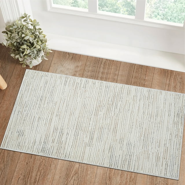 Modern beige cream indoor area rug with abstract textured pattern displayed on wood flooring by a window and potted plant.