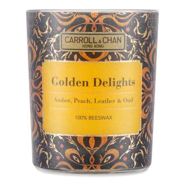 vela votiva Carroll & Chan 100% cera de abejas Golden Delights multicolor en tarro de vidrio decorativo frontal con etiqueta amarilla que lee "Golden Delights" y notas "Amber, Peach, Leather & Oud", patrón ornamental marrón y dorado, mecha de algodón centrada; adecuada como pieza aromática decorativa para habitaciones pequeñas.