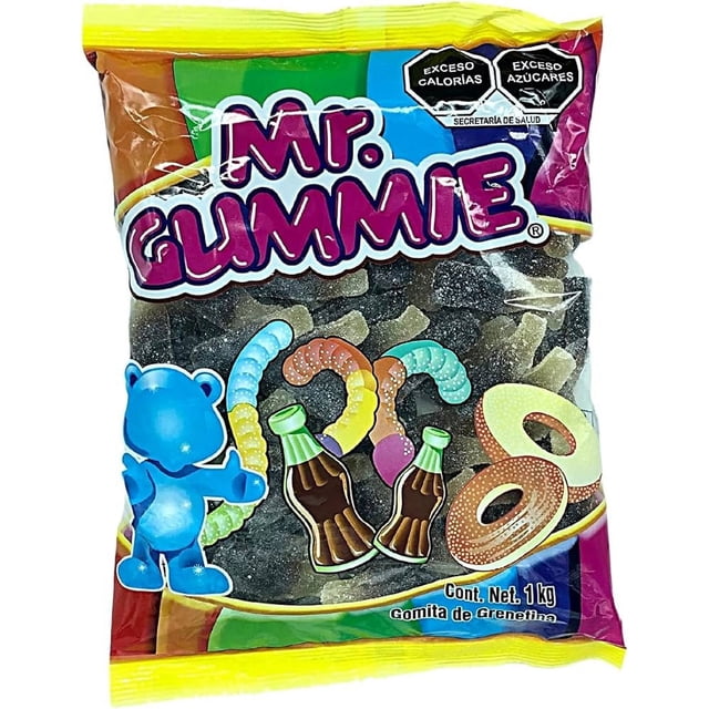 gomitas sabor cola cuetara - mr. gummie 2 kg Paquete frontal que indica 2 kg (dos bolsas de 1 kg) de gomitas sabor refresco de cola Mr. Gummie; vista centrada y frontal con logo 'Mr. Gummie', etiquetas de exceso de calorías y azúcares, ilustraciones de osito azul y botellas de cola; se aprecian gomitas alargadas y anillos oscuros con revestimiento granular visibles a través del empaque. Suelen usarse también para decorar postres o mesas de fiesta.