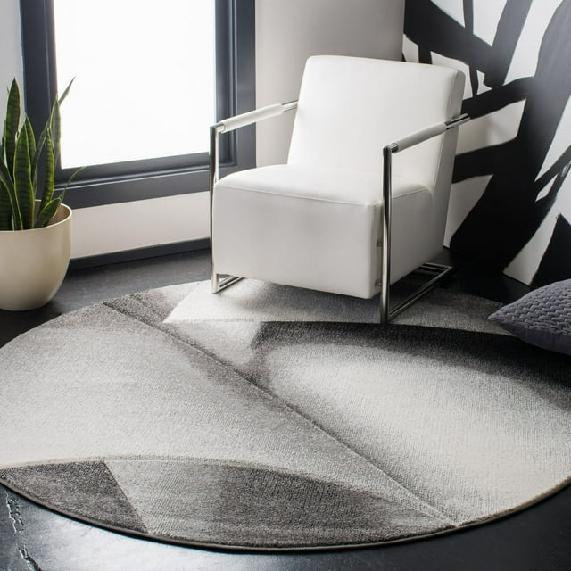 Safavieh Hollywood Salome Abstract Area Rug, round with mid-century modern geometric pattern in grey and white, placed under a white armchair with chrome frame in a contemporary room with black and white wall art and a potted snake plant, ideal for accenting modern living spaces.