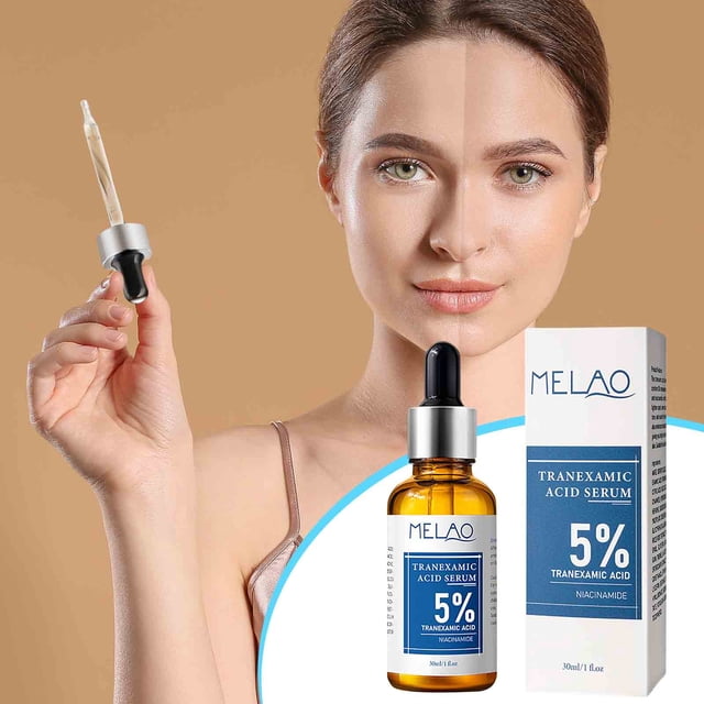 esencia tranexámica aclarante e iluminadora del tono de la piel 30ml esencia esencia Vista frontal de frasco de vidrio ámbar de 30 ml con etiqueta azul y caja a juego; frasco con collar plateado y pipeta con capuchón negro sostenida hacia la izquierda y suero transparente visible sobre fondo beige con torso de modelo recortado. Textura ligera y de rápida absorción según especificaciones; a menudo usada como suero diario antes de crema hidratante.