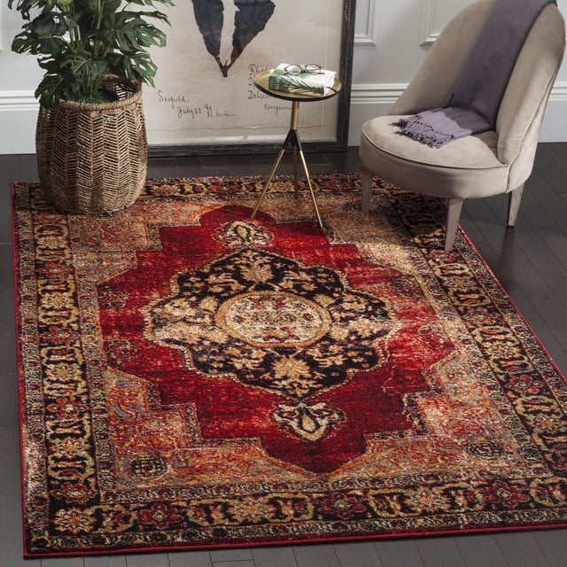 Vintage-style SAFAVIEH Hamadan Tahnee traditional area rug featuring intricate red, black, and beige patterns on dark hardwood flooring beside a modern chair with gray throw blanket and gold tripod side table.