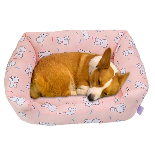 cama refrescante para perros, de seda fría y transpirable, ideal para perros y gatos pequeños, medianos y grandes, con base antideslizante. Vista frontal centrada de una cama acolchada rosa con estampado de conejos y bordes elevados en forma rectangular; perro pequeño durmiendo enrollado en el interior. Tela de nailon de contacto frío (textura lisa) indicada en la etiqueta y base con puntos antideslizantes; colores brillantes adecuados para verano. Suele usarse también como cama portátil para mascotas pequeñas.