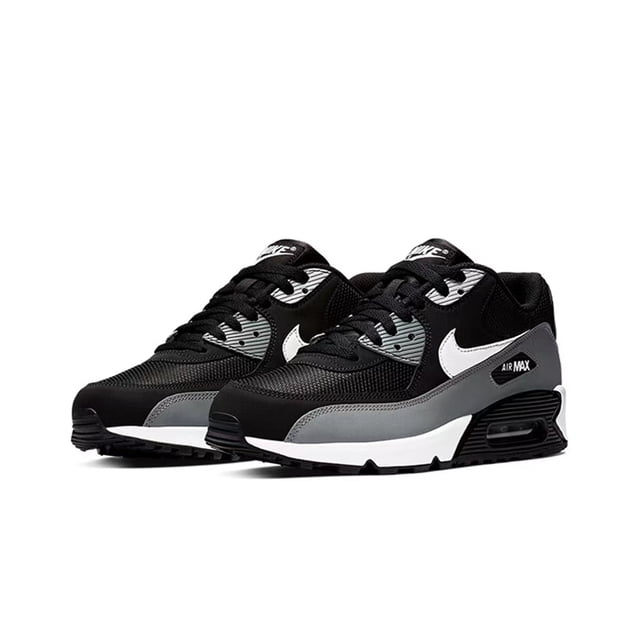 zapatillas deportivas Air Max 90 de piel, color negro, gris y blanco, caña baja unisex; vista 3/4 frontal de par sobre fondo blanco, empeine de malla con paneles de PVC gris, logo lateral blanco, mediasuela blanca con unidad Air Max visible y suela EVA negra, cierre con cordones y ajuste a talla real. Adecuadas para running de nivel principiante y uso casual; también suelen usarse para caminatas cortas en césped al aire libre.