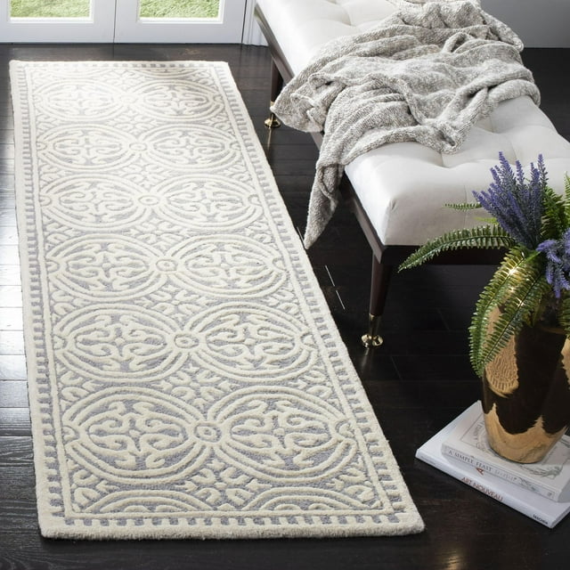 SAFAVIEH Cambridge Leslie runner rug featuring raised geometric circular patterns in light gray and cream tones on a dark hardwood floor next to a white bench with a textured throw blanket and decorative plant