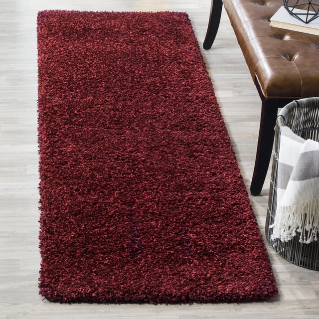 Deep red plush shag area rug from Safavieh California collection placed on a light wood floor beside a brown leather bench and woven basket with striped blanket.