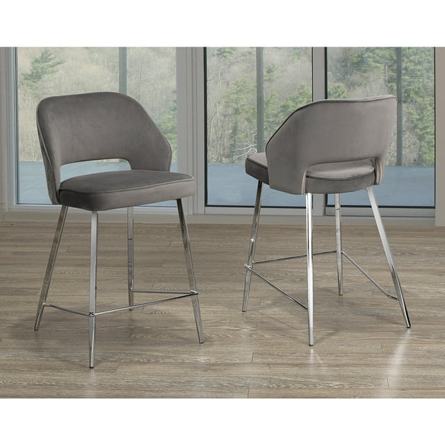 COSMIC HOMES COUNTER STOOL, SET OF 2 - GREY VELVET, KITCHEN STOOL. A set of two contemporary counter-height stools with a neutral grey velvet fabric cover and chrome-finished splayed legs. The stools feature contoured chair backs and plush seating for comfort, making them ideal for kitchen or bar areas. Shown in a modern interior with a wood floor and large windows in the background.