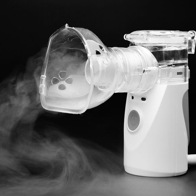 nebulizador portátil compacto, diseño ergonómico para uso en casa o viaje, carga usb, niebla fina, ideal para niños y adultos, color gris — Vista frontal 3/4 de un nebulizador gris con mascarilla y boquilla transparentes conectadas, botón de encendido visible y niebla fina saliendo de la mascarilla; tamaño de mano, recargable por USB, pulverización precisa, fácil de transportar para hogar y viajes y a menudo usado para nebulizar soluciones salinas no médicas durante traslados.