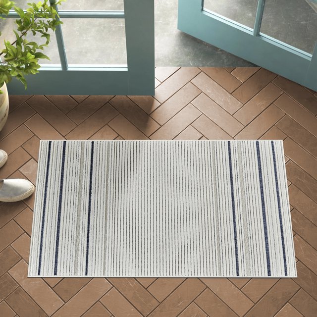 Modern rectangular indoor outdoor area rug with cream base and blue vertical stripes placed on brown herringbone tile floor by open teal double doors.