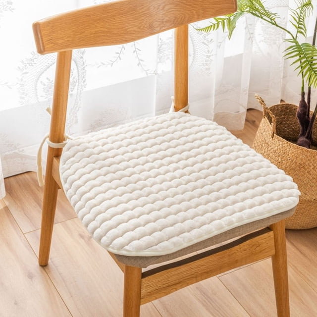funda de almohada universal de felpa para silla, cojín para silla, cojín para taburete de comedor, cojín para taburete de entrada, cojín para asiento, cojín de felpa aterciopelada blanco 47x45 cm en vista 3/4 sobre una silla de madera; superficie acolchada en franjas con textura de flock suave, lazos laterales para atar y base lisa, ambiente de comedor luminoso con cortina y maceta; también apto como asiento extra para sentarse en el suelo.