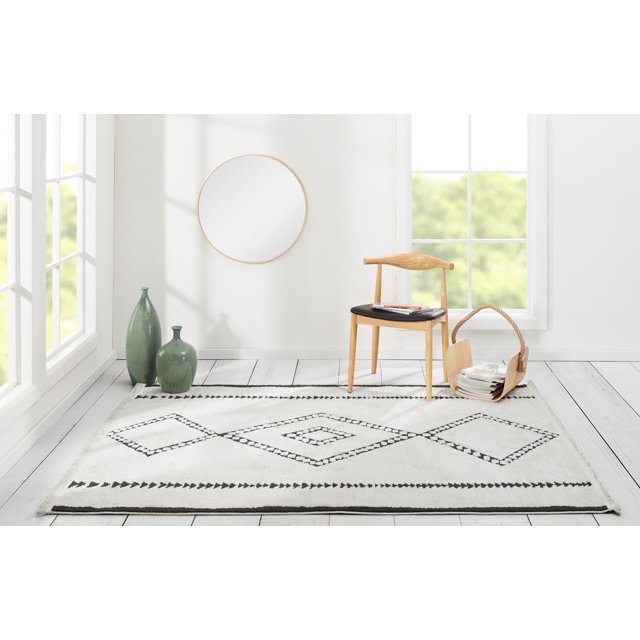 ECARPET Zelda Contemporary Area Rug with southwestern tribal black diamond patterns on ivory, set on white wooden floor in a bright room with large windows, a wooden chair with black seat cushion holding books, two green ceramic vases, and a woven basket with magazines, suitable for living rooms, bedrooms, and hallways.
