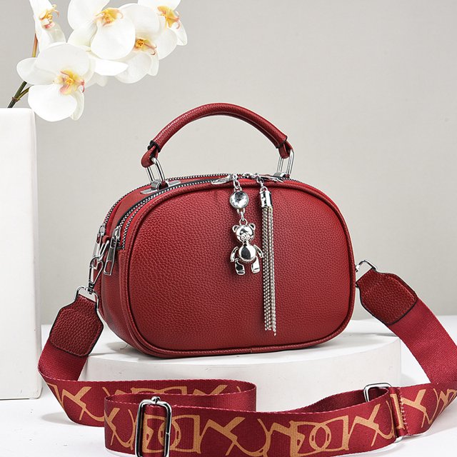 bolso de mano de diseñador de moda para mujer bolso de hombro de cuero para mujer bolso cruzado clásico para mujer bolso cuadrado pequeño con borlas para mujer — Bolso cuadrado pequeño de PU rojo en vista 3/4 frontal con asa superior y correa ancha ajustable; doble cremallera, textura granulada, colgante metálico tipo oso y borla, herrajes plateados, interior con bolsillo ranura y bolsillo para teléfono, apto para uso casual y como bandolera ligera.