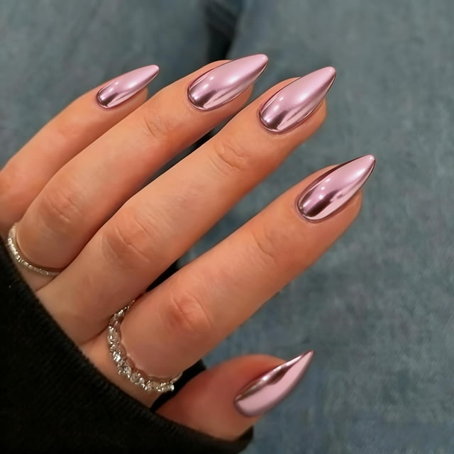 uñas cromadas de color rosa claro, uñas medianas de almendra, pegamento metálico, uñas acrílicas, uñas postizas para mujeres, pegamento falso grueso y brillante en uñas de longitud media, 24 unidades Mano en vista 3/4 con uñas postizas almendradas de largo medio en acabado espejo rosa claro, superficie metálica brillante y contornos definidos; fondo azul grisáceo y anillos plateados; suele usarse para manicuras rápidas y looks formales.