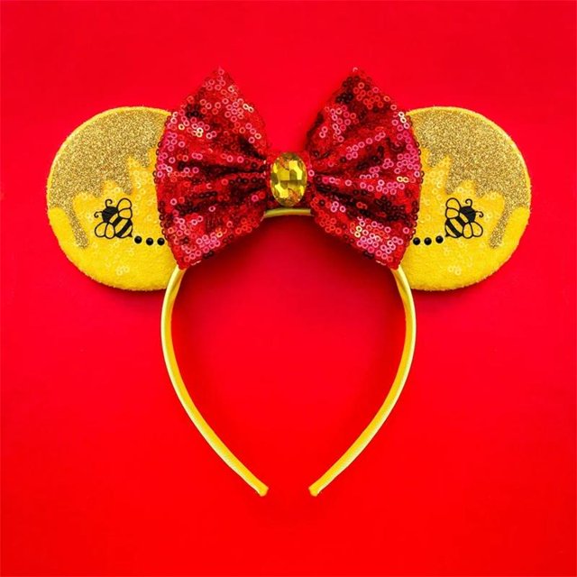diadema de oreja de mickey minnie winnie the pooh disfraz de orejas de lentejuelas cosplay adultos niños halloween regalo diadema amarilla, vista frontal centrada con orejas redondas cubiertas de lentejuelas doradas y siluetas de abeja impresas; lazo rojo de lentejuelas con gema ovalada en el centro, sobre fondo rojo. Adecuada para disfraces, fiestas o sesiones de fotografía.