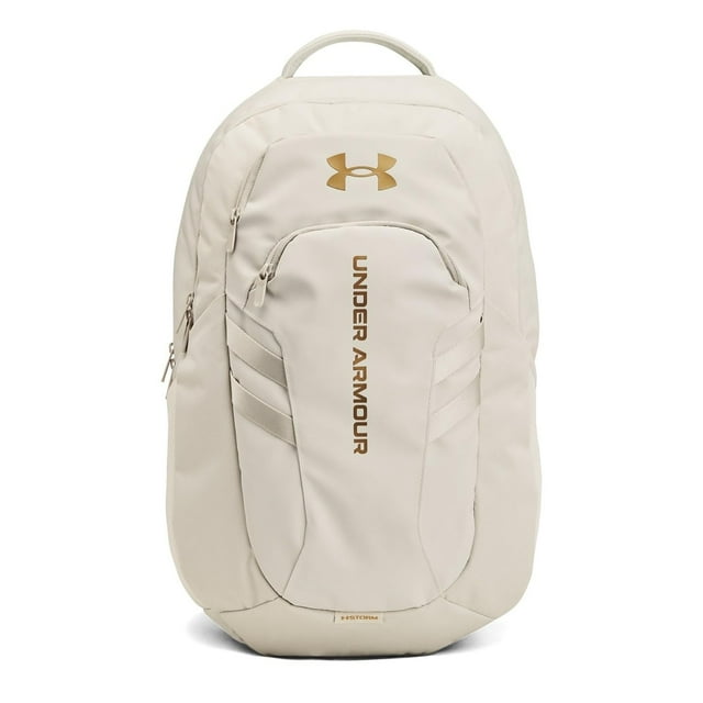 mochila under armour hustle 6.0 pro summit blanco oro frontal, mochila unisex talla única blanco summit con logo y texto Under Armour en dorado metálico, silueta estructurada con compartimento frontal acolchado, cremalleras visibles y asa superior; suele usarse para deporte, escuela y uso diario.