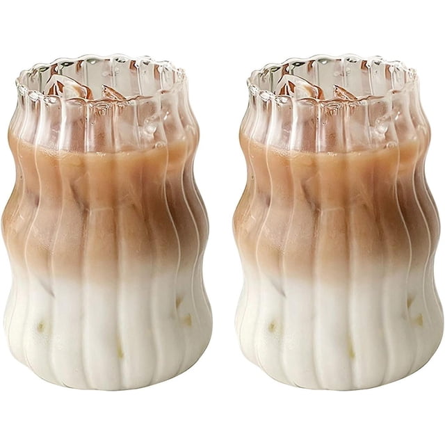 vasos para beber de cristalería acanalados, 2 uds., set de vasos de vidrio ondulado con forma de calabaza de 18 oz (530 ml), vista frontal 3/4 con ambos vasos llenos de café helado bicolor; vidrio transparente con paredes acanaladas y borde superior ondulado tipo origami, base redondeada y diseño vintage europeo, aptos para bebidas frías y calientes y a menudo usados también para servir postres fríos en reuniones.