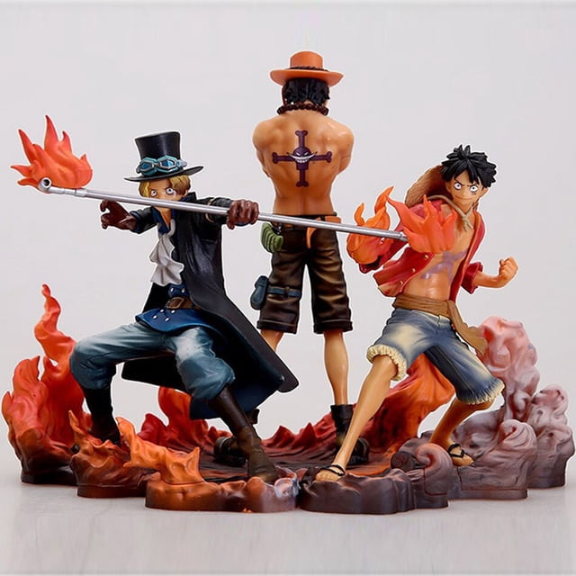 figuras de acción de one piece, set de 3 piezas Monkey D. Luffy Ace Sabo modelo coleccionable de PVC 14-17cm. Vista 3/4 frontal con los tres personajes sobre una base con llamas: Luffy a la derecha con chaqueta roja, pantalón corto azul y efecto de fuego en el puño; Ace en el centro de espaldas con sombrero naranja y tatuaje en la espalda; Sabo a la izquierda con abrigo negro, sombrero alto y bastón largo; detalles de pintura y sculpt en PVC, embalaje: con caja o bolsa OPP; adecuado para exhibición coleccionable.