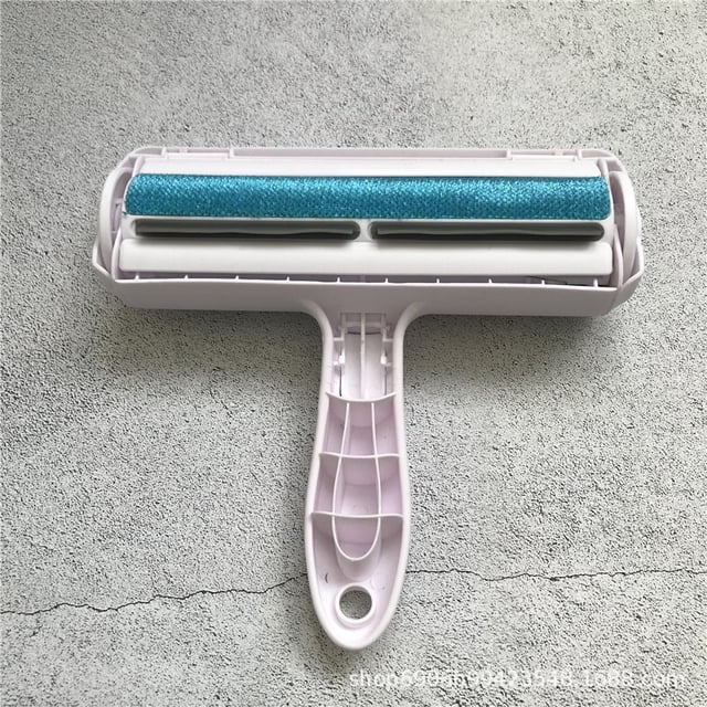 rodillo removedor de pelo de mascotas - removedor de pelo de perros y gatos con base de autolimpieza - herramienta eficiente de eliminación de pelo de animales sincero hogar. Vista cenital frontal del rodillo reutilizable con mango ergonómico y cabezal ancho; rodillo texturizado azul que recoge el pelo, carcasa plástica color claro y depósito interno accesible al abrir la tapa, sobre superficie gris. Apto para limpieza de muebles y telas según especificaciones; a menudo se usa también para recoger pelo en cojines y fundas durante viajes.