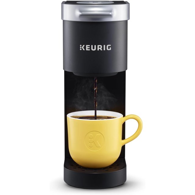 cafetera keurig k-mini® monodosis k-cup color negro mate certificado restaurado, vista frontal centrada de la cafetera compacta dispensando café en una taza; cuerpo negro mate con logo Keurig, bandeja de goteo extraíble que acepta tazas hasta 7.0 pulgadas, depósito de una taza y base de menos de 5 pulgadas ideal para espacios pequeños; suele usarse también para preparar una sola taza rápida en oficinas o habitaciones pequeñas.