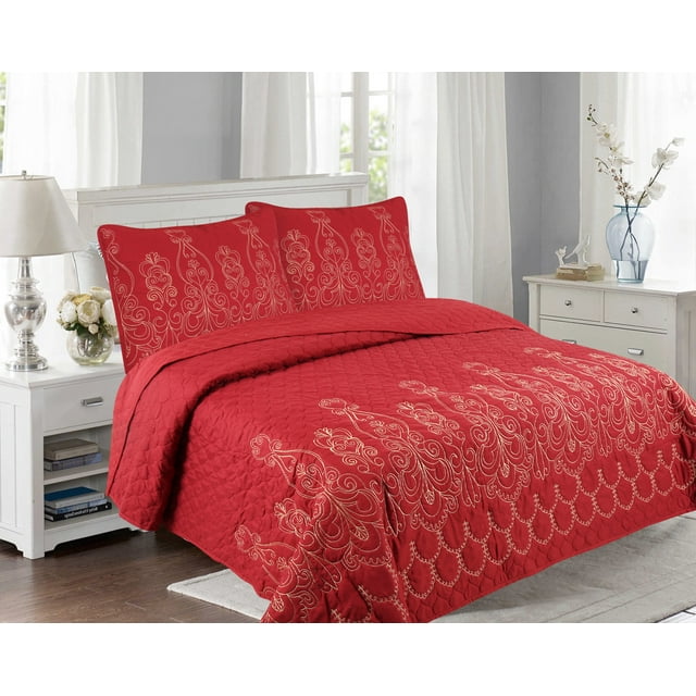 Red embroidered quilt set with gold floral stitching, including coverlet and pillow shams, displayed on a white bed in a modern bedroom.