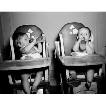 Two babies sitting in high chairs drinking from baby bottles Stretched Canvas -  (24 x