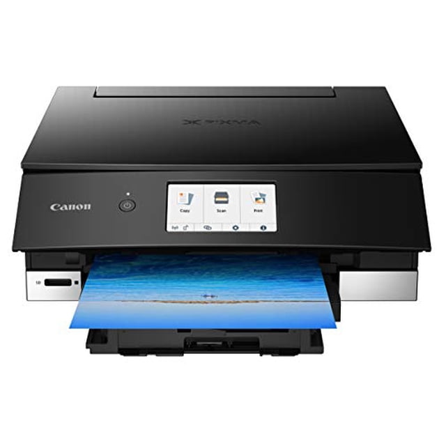 impresora fotográfica multifunción inalámbrica canon ts8220 con escáner y fotocopiadora, impresión móvil, color negro, compatible con alexa vista frontal centrada de la PIXMA TS8220 en negro con bandeja frontal abierta y una foto impresa saliendo; pantalla táctil LCD 4.3" visible con iconos de copiar, escanear e imprimir, logo Canon a la izquierda y ranura para tarjeta en el frente. Compatible con AirPrint, Mopria y Bluetooth; suele usarse también para imprimir fotografías de viaje y proyectos domésticos.
