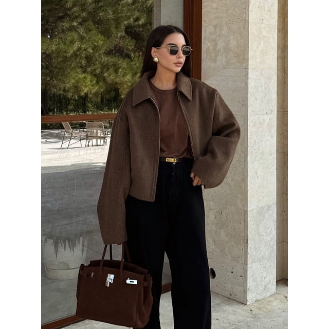 chaqueta corta de lana marrón vintage para mujer chaqueta corta de corte recortado con cremallera, manga larga y solapa elegante; tejido de poliéster con textura marrón khaki, silueta cuadrada hasta la cadera, hombros caídos y cierre frontal visible en vista 3/4 exterior sobre fondo de piedra y vidrio; a menudo se usa como prenda de calle combinable con pantalones de talle alto.