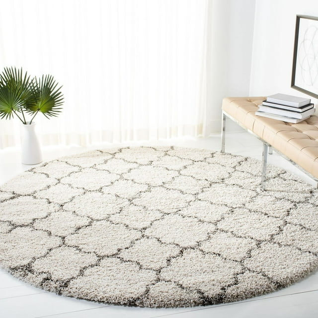 Round Safavieh Hudson Jaye shag area rug featuring a beige background with dark brown geometric trellis design, placed on white floor near bench and plant.