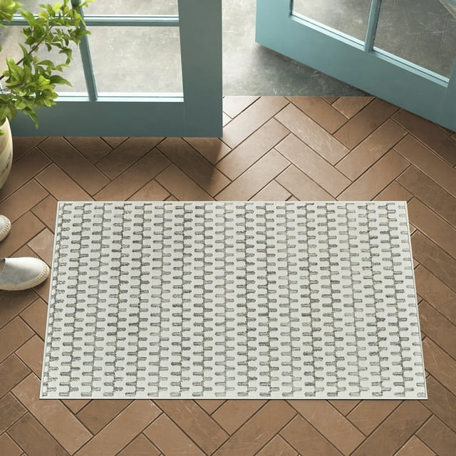 Cream beige Rug Branch Maise abstract indoor outdoor area rug with modern branch design on brown herringbone tile floor by open blue door and green plant.