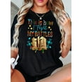 thumbnail image 1 of Camiseta gráfica informal para mujer: "Así lucho mis batallas" con diseño floral y libro. Cómoda camiseta de verano de manga corta. Camiseta negra de mezcla de algodón para un look informal. Camisetas, 1 of 8