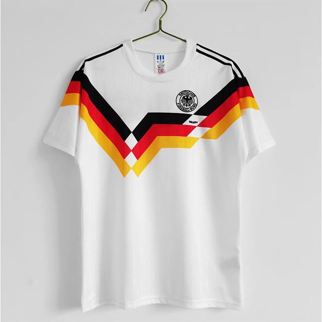 camiseta de fútbol clásica de verano de alemania de manga corta, blanca, 1990xl frontal centrada; camiseta blanca con cuello redondo, franjas en V negras, rojas y amarillas en el pecho que replican el diseño de Alemania 1990, escudo circular impreso en el pecho izquierdo y tres líneas negras en los hombros; colgada sobre gancho en fondo neutro; adecuada como top casual vintage.